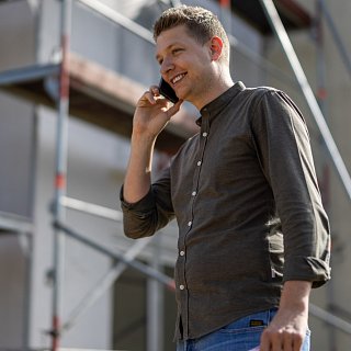Mann telefoniert und steht vor einem Haus mit Baugerüst