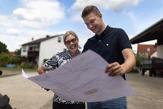 Zwei Personen stehen im Freien und blicken auf einen Bauplan