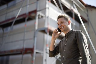 Mann steht telefonierend vor einem Haus mit Baugerüst